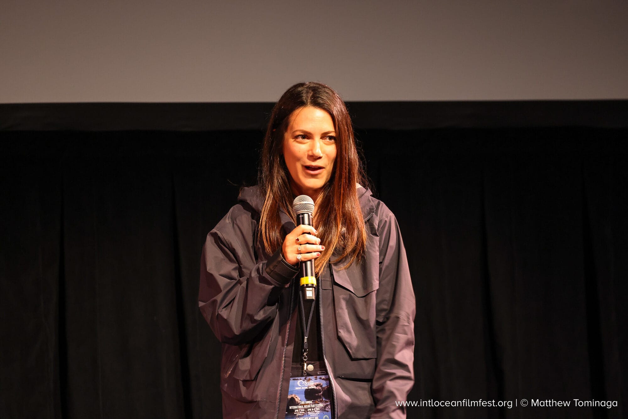 Andi Cross speaking into a microphone on stage at the International Ocean Film Festival
