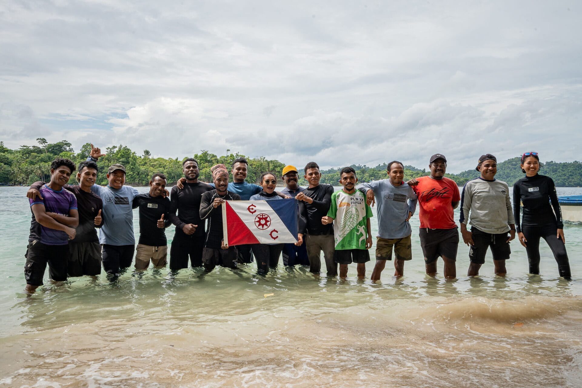 Expedition team in Misool, Indonesia, standing in shallow water holding dive flags and celebrating a conservation partnership